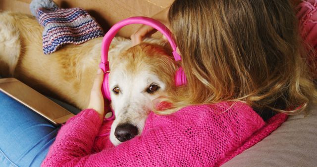 Young girl relaxing on a couch with her dog, who is wearing pink headphones, providing a cozy and casual home setting. Excellent visual for themes related to pet companionship, leisure activities, and cozy domestic life. Ideal for use in lifestyle blogs, pet care promotions, and advertisements encouraging bonding time with pets.