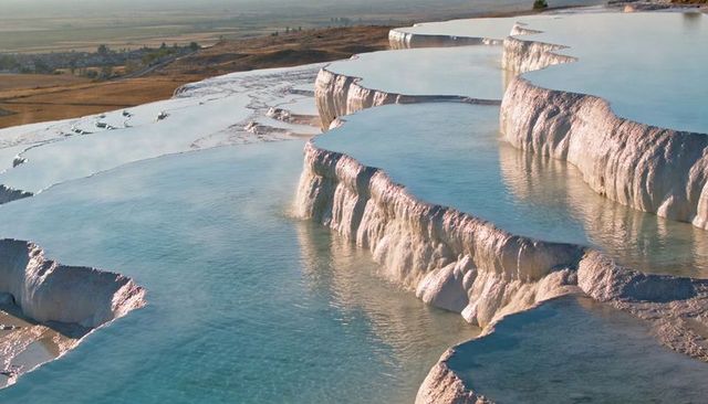 Sunlit travertine terraces cascading with turquoise pools on limestone plateau