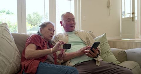 Senior couple making mobile payment on couch with credit card and smartphone at home
