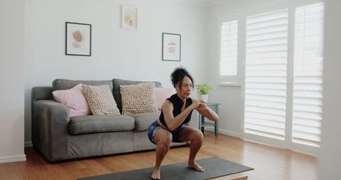 Woman doing squats on yoga mat in bright minimalist living room for home workout