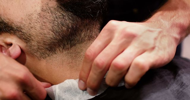 Male customer receiving a haircut at barber shop. Barber applying neck strip for hygiene before haircut. Useful for articles about men's grooming, barber techniques, hairdressing, and personal hygiene practices.