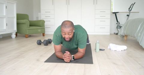 African american man holding plank on mat in bright minimalist bedroom home workout