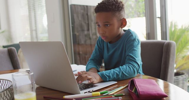African American boy intently using laptop at home. Appears to engage in educational activity or remote learning. Useful for content about home schooling, education during digital age, studying environments, or technology use by children.
