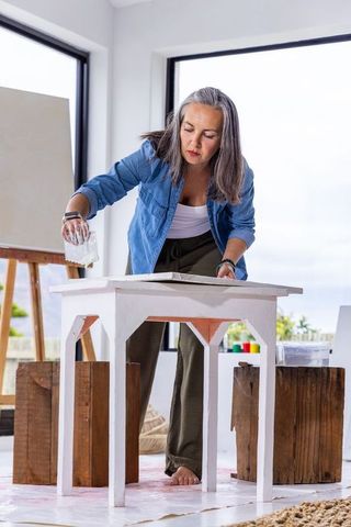 Senior woman refinishing wooden table with sponge in bright home studio, diy project