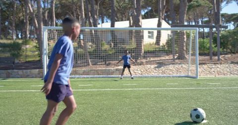 Youth soccer teammates running toward ball on sunny artificial turf goalkeeper defending