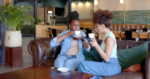 Friends chatting over coffee on brown leather sofa in cozy rustic cafe