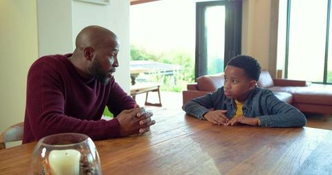 African american father talking with son at dining table during heartfelt conversation