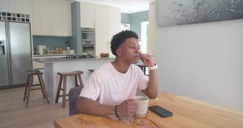 African American man contemplating with coffee at modern sunlit kitchen table