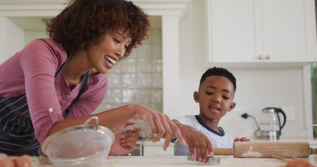 This image of a mother and her son baking in the kitchen can be used for family-oriented content, blogs about parenting or cooking with children, advertisements for household products, and educational materials about family activities.