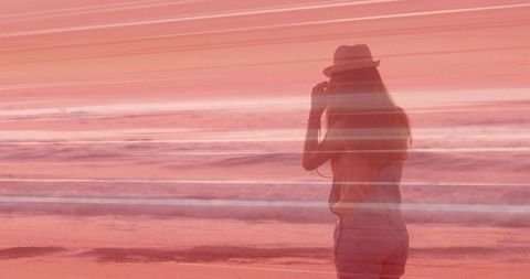 Silhouetted woman capturing pastel seaside sunset with horizontal light streaks