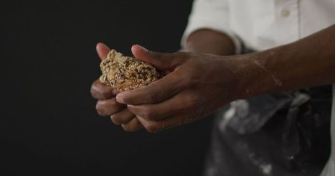Hands holding freshly baked multigrain loaf on black background