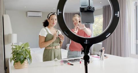 Diverse female friends filming makeup tutorial together at home
