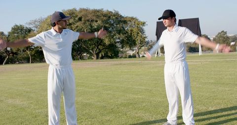 Diverse cricket teammates stretching and warming up in white kit on sunlit grass field