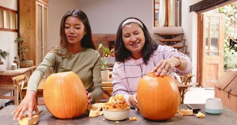 Grandmother and Granddaughter Carving Pumpkins for Halloween at Home