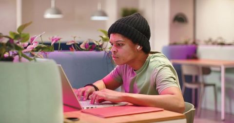 Focused young man typing on laptop in modern coworking space with ambient pink lighting