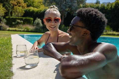 Diverse couple relaxing at backyard poolside on sunny day