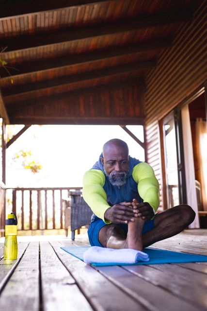 Bald african american senior man stretching body while sitting on exercise mat at log cabin - Download Free Stock Photos Pikwizard.com