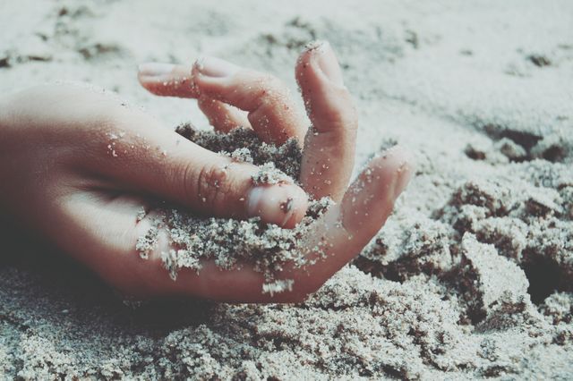 A close-up view of a hand grasping sandy beach. This can be used for themes such as relaxation, nature, or summer recreation. Potential use cases include travel blogs, wellness and relaxation promotions, nature and beach resort advertisements.