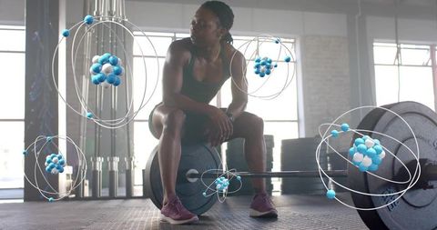 Female athlete sitting on loaded barbell in gym with atom science overlays for strength