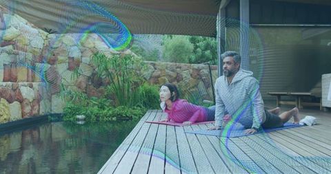 Couple practicing yoga backbend on wooden deck beside pond garden patio morning