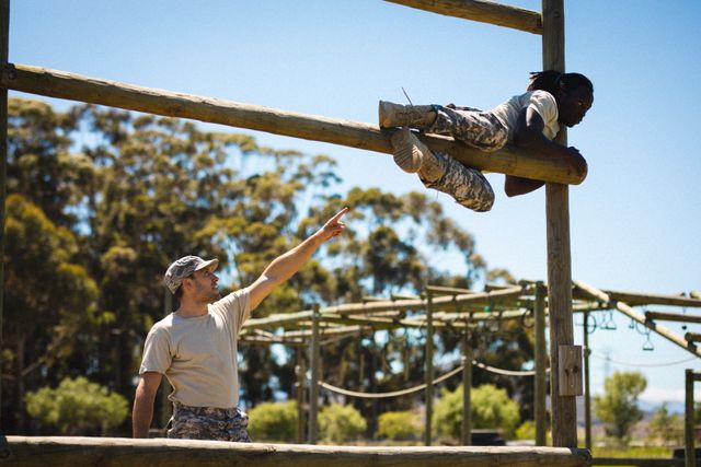 Soldiers participating in a military training obstacle course. One soldier is guiding another as he crosses a wooden obstacle. This image can be used to depict military training, teamwork, physical fitness, and discipline. It is suitable for articles, advertisements, and educational materials related to military training and physical endurance.