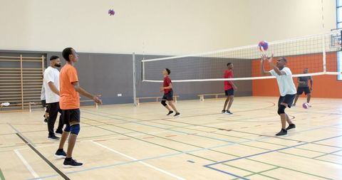 Diverse men playing indoor volleyball with african american player preparing to set at net