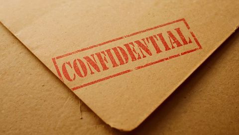 Diagonal kraft envelope with red confidential stamp on textured cardboard surface