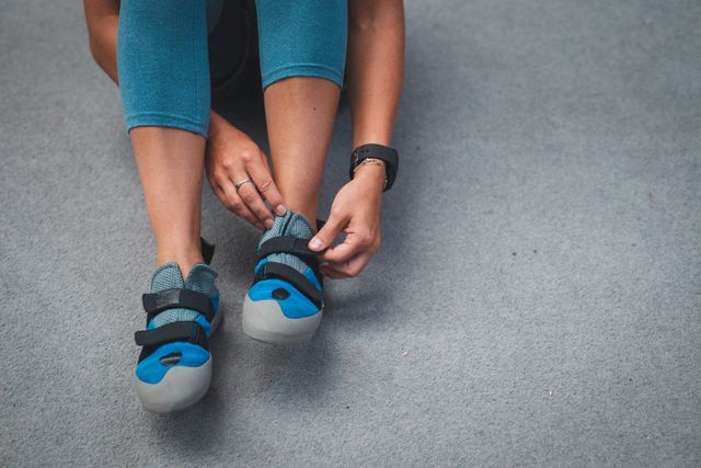 This image shows a woman preparing for indoor climbing by putting on her climbing shoes. Ideal for use in articles or advertisements related to fitness, climbing, sports gear, and active lifestyles. It can also be used in blogs or social media posts about climbing tips, preparation, and indoor sports activities.