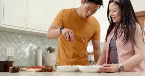 Young couple preparing fresh salad with cherry tomato on bright modern kitchen countertop