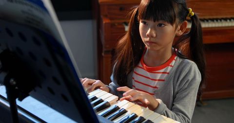 Young Asian Girl Practicing Piano with Focus