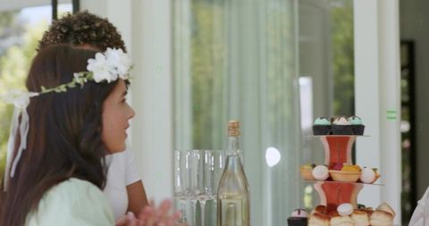 Clapping woman celebrating at sunlit garden brunch with floral headband and desserts