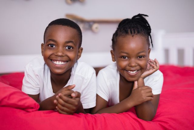 Portrait of smiling siblings lying together on bed at home