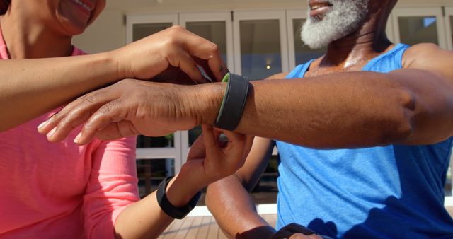 Senior man receiving help adjusting a fitness tracker outdoors, promoting fitness and health awareness. The image can be used for fitness equipment advertisements, wellness programs targeted at seniors, health magazines, or fitness blogs focusing on active and healthy lifestyles for older adults.