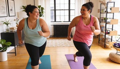 Friends doing home workout lunges on yoga mats, laughing and syncing rep counter with music