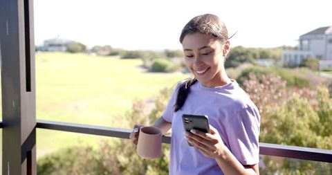 Woman Smiling with Smartphone and Coffee on Balcony