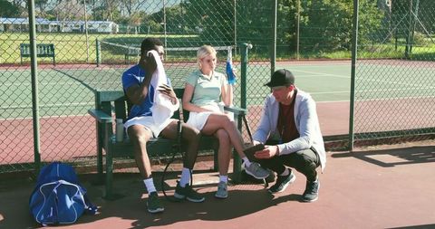 Coach reviewing tablet with tennis players during break on sunlit outdoor court