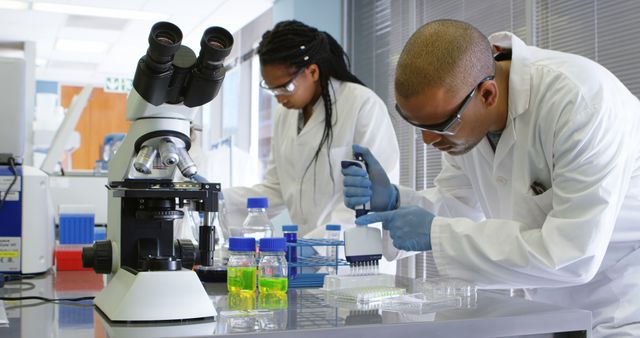 Researchers dressed in lab coats and safety glasses conducting experiments in a high-tech laboratory. Laboratory equipment including beakers, test tubes, and a microscope are prominently displayed. This visual is ideal for use in educational materials, scientific publications, healthcare advertising, technology presentations, and academic research promotion.