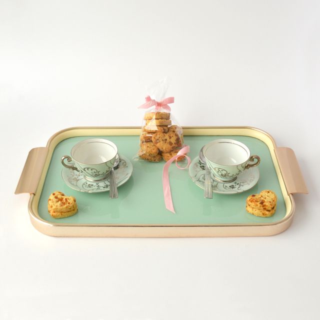 Elegant tea set with cups and saucers on a pastel green serving tray, accompanied by cookies wrapped with a ribbon. Perfect for use in marketing tea products, elegant dining, hospitality services, and special occasions.