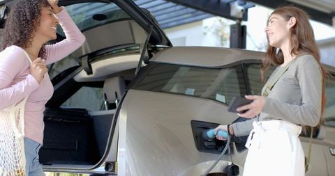 Diverse females charging electric vehicle in home carport environment