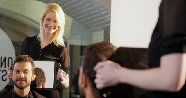 Barber presenting freshly cut hairstyle to male client using handheld mirror - Download Free Stock Images Pikwizard.com