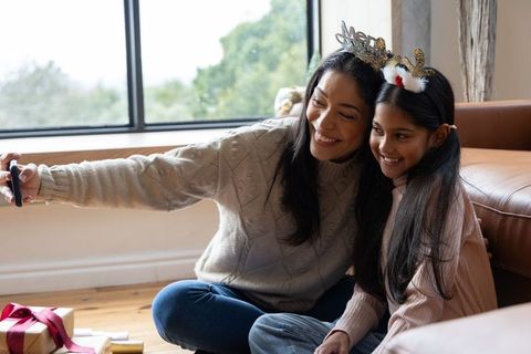 Joyful mother and daughter taking selfie while unwrapping holiday presents at home
