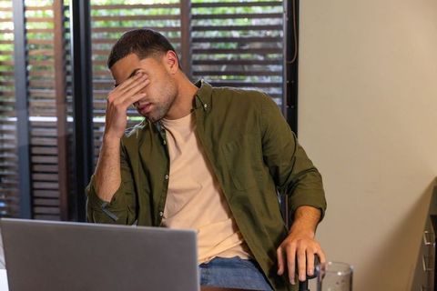 Stressed man rubbing eyes at home workspace with laptop