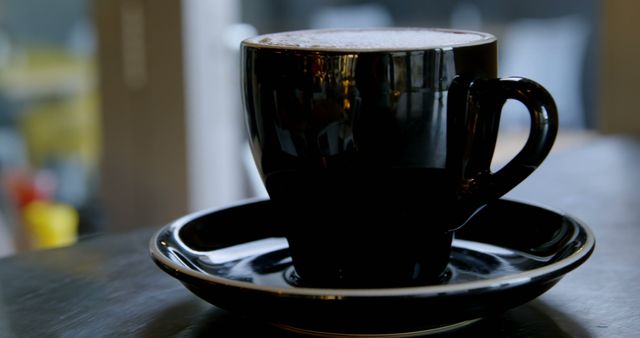 A steaming cup of coffee is presented in a black cup on a saucer, suggesting a moment of relaxation or a coffee break. The frothy top indicates it could be a cappuccino or latte, popular choices for coffee enthusiasts.