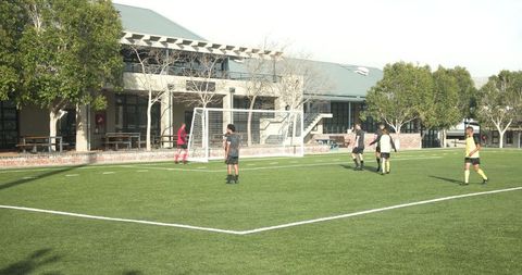 Teenagers playing soccer on school field under clear sky