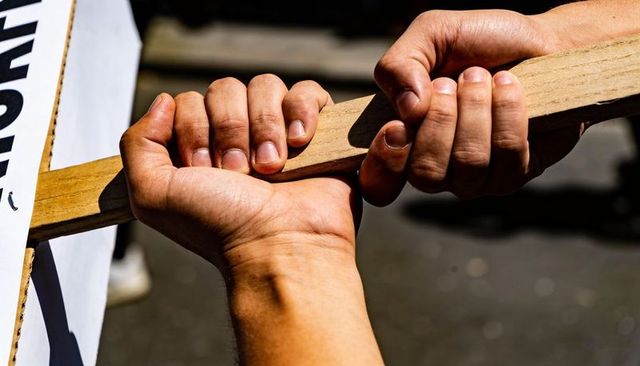 Hands gripping wooden placard handle showing solidarity and teamwork during protest