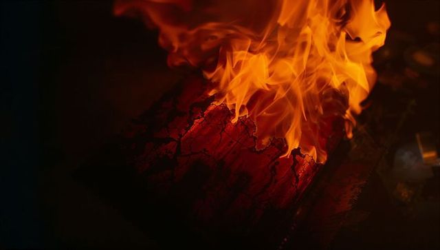 Intense Flames Engulfing Charred Wooden Plank in Low Light
