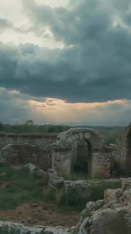 Vertical cinematic storm clouds parting with sunbeams over ancient stone arch and ruins