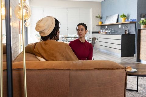 African american couple talking on leather sofa in modern cozy open-plan living space