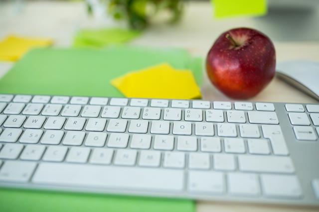 Close-up of a keyboard with apple on desk in office