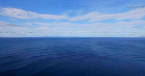Open ocean stretching to straight horizon with distant island and layered clouds